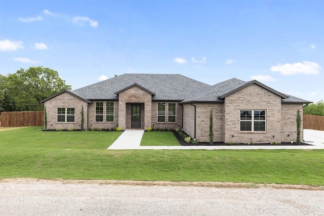 view of front of house featuring brick siding, a shingled roof, a front lawn, and fence