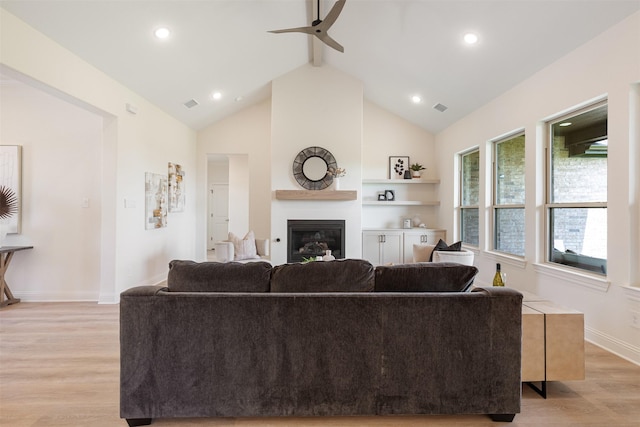 living area featuring a ceiling fan, visible vents, beam ceiling, light wood finished floors, and a glass covered fireplace