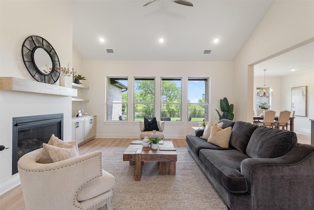 living area with a glass covered fireplace, visible vents, light wood-type flooring, and lofted ceiling