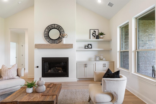 living area featuring visible vents, a glass covered fireplace, lofted ceiling, and light wood-type flooring