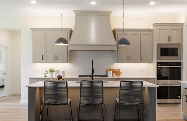 kitchen featuring stainless steel double oven, light countertops, built in microwave, premium range hood, and a center island with sink