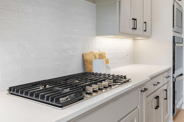 kitchen with light countertops, backsplash, white cabinets, and stainless steel appliances