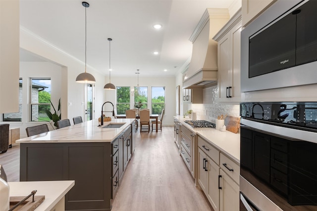 kitchen featuring appliances with stainless steel finishes, a sink, light wood-style floors, decorative backsplash, and custom range hood