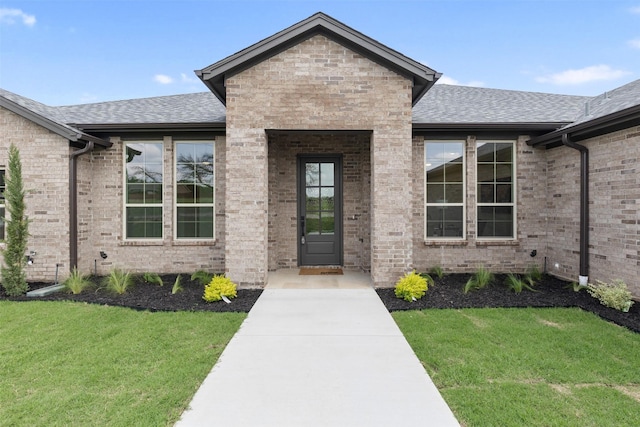 doorway to property featuring brick siding, a shingled roof, and a yard