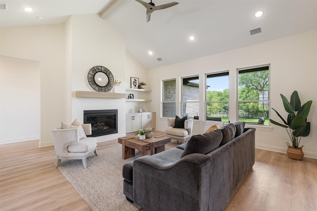 living room featuring visible vents, a glass covered fireplace, baseboards, high vaulted ceiling, and light wood-type flooring