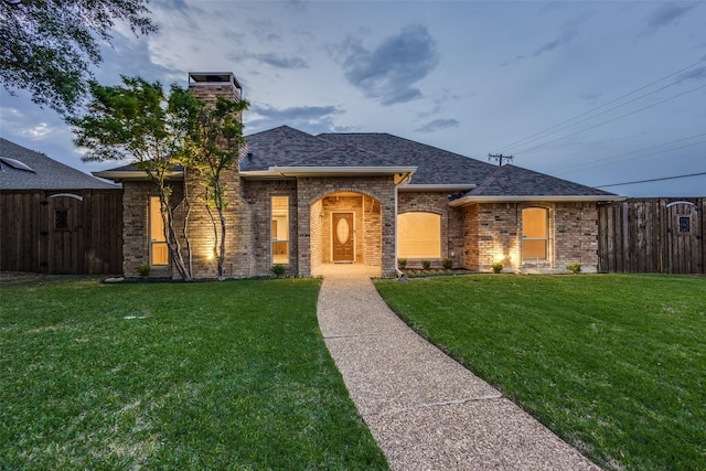 ranch-style home with brick siding, fence, a shingled roof, and a front lawn