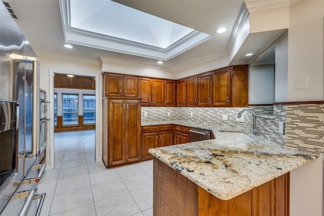kitchen with brown cabinetry, a raised ceiling, light stone counters, a sink, and stainless steel appliances