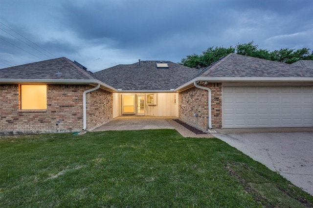 back of house featuring a shingled roof, brick siding, a garage, concrete driveway, and a yard