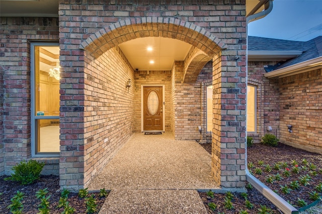 doorway to property with brick siding and roof with shingles
