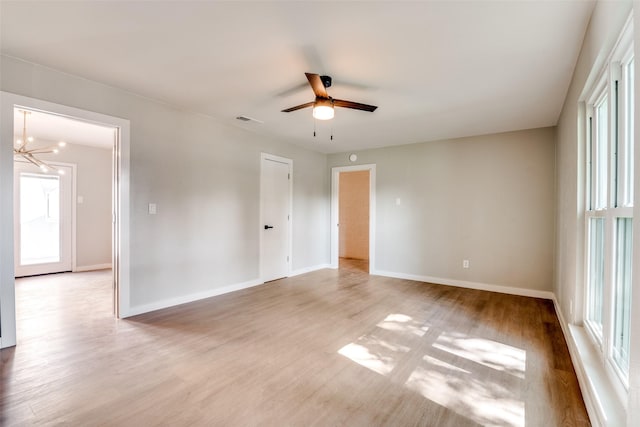 spare room featuring visible vents, light wood finished floors, ceiling fan with notable chandelier, and baseboards