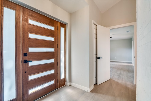 foyer entrance featuring baseboards, light wood-style flooring, and lofted ceiling