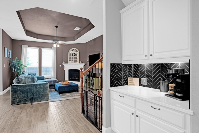 bar area featuring backsplash, a tray ceiling, ceiling fan, baseboards, and light wood-type flooring
