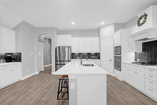 kitchen featuring stainless steel appliances, a sink, tasteful backsplash, arched walkways, and a kitchen bar