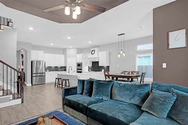 living room featuring ceiling fan, stairway, light wood-style flooring, recessed lighting, and baseboards