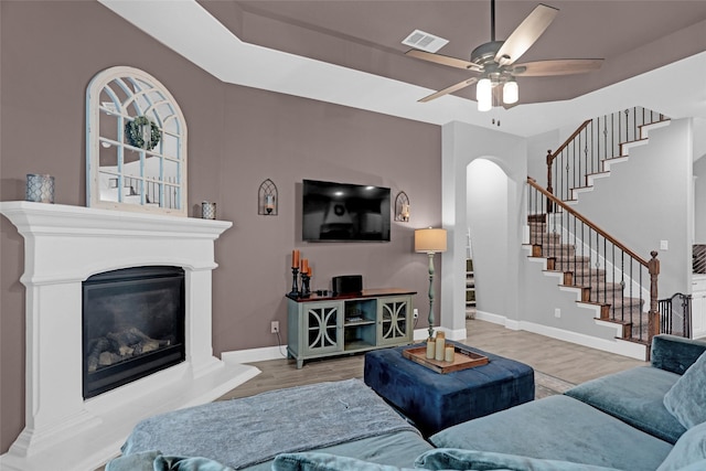 living area with wood finished floors, a glass covered fireplace, stairs, arched walkways, and a ceiling fan