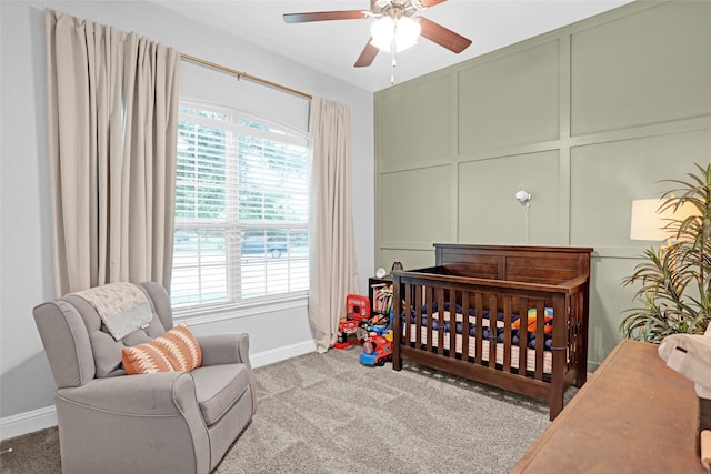 bedroom with a crib, baseboards, carpet, a decorative wall, and a ceiling fan
