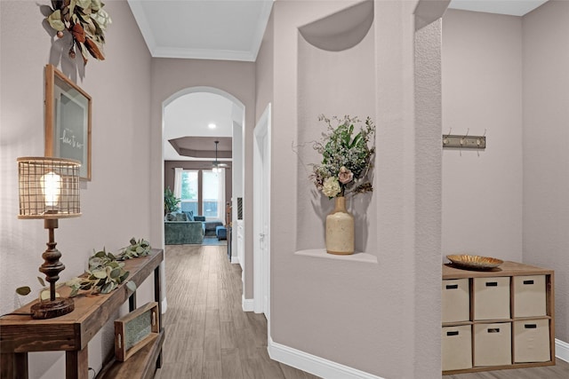 hallway featuring arched walkways, wood finished floors, ornamental molding, and baseboards