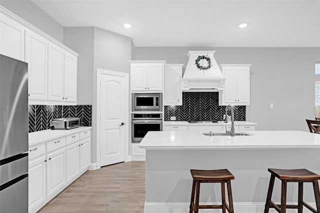 kitchen with appliances with stainless steel finishes, a sink, a kitchen breakfast bar, premium range hood, and white cabinetry