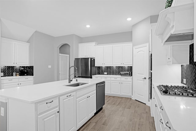 kitchen featuring stainless steel appliances, a sink, backsplash, arched walkways, and recessed lighting