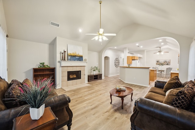 living area featuring visible vents, a fireplace, ceiling fan, light wood-type flooring, and arched walkways