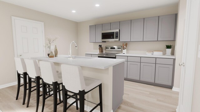 kitchen featuring appliances with stainless steel finishes, a sink, gray cabinetry, light wood finished floors, and recessed lighting