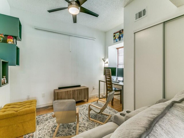 interior space featuring a ceiling fan, a textured ceiling, visible vents, and wood finished floors