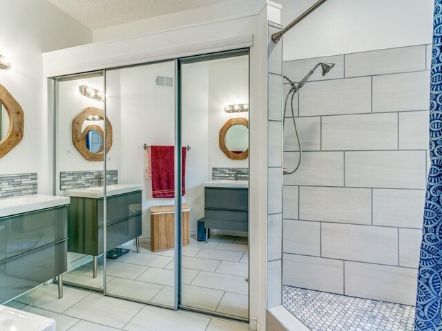 full bathroom featuring vanity, visible vents, tiled shower, tile patterned floors, and tasteful backsplash