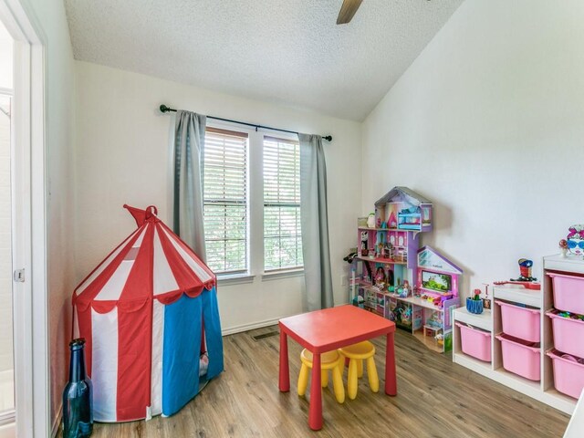 game room with a ceiling fan, a textured ceiling, wood finished floors, and vaulted ceiling