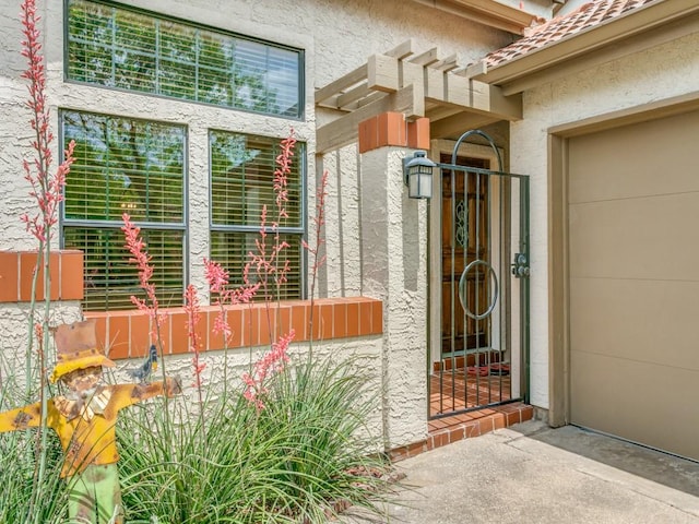 view of exterior entry featuring a garage, a gate, and stucco siding