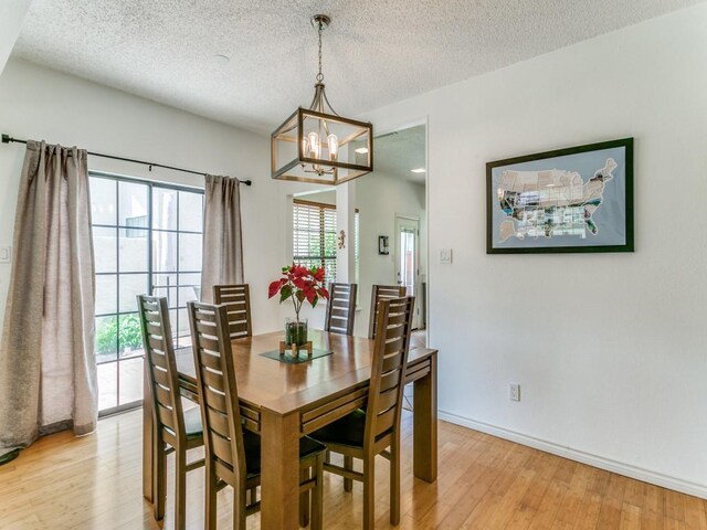 dining space with baseboards, light wood-type flooring, a textured ceiling, and a notable chandelier