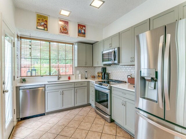 kitchen featuring gray cabinets, a textured ceiling, a sink, light countertops, and stainless steel appliances