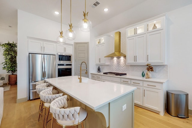 kitchen featuring light wood-style flooring, wall chimney exhaust hood, stainless steel appliances, decorative backsplash, and visible vents