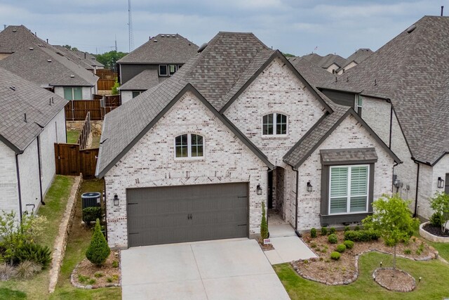 french country inspired facade featuring roof with shingles, fence, driveway, and brick siding