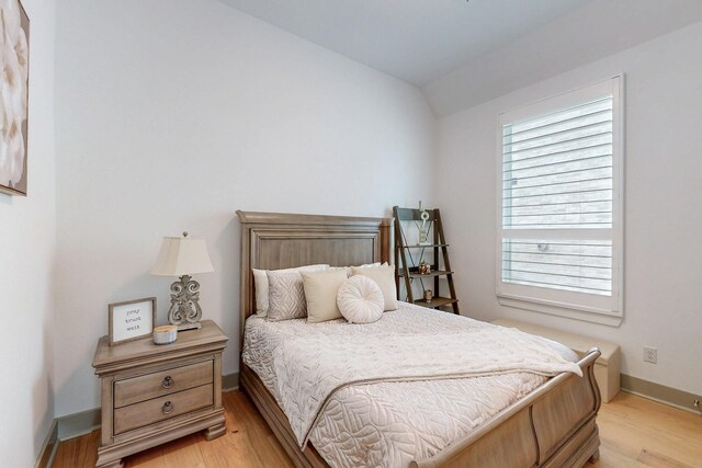 bedroom featuring baseboards, light wood-style flooring, and lofted ceiling