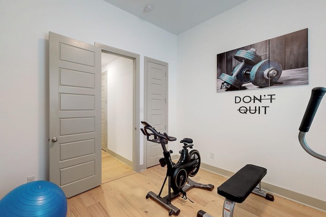 exercise room featuring baseboards and light wood finished floors