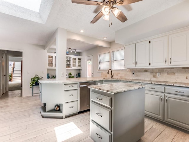 kitchen with stainless steel dishwasher, a center island, gray cabinets, a sink, and a textured ceiling