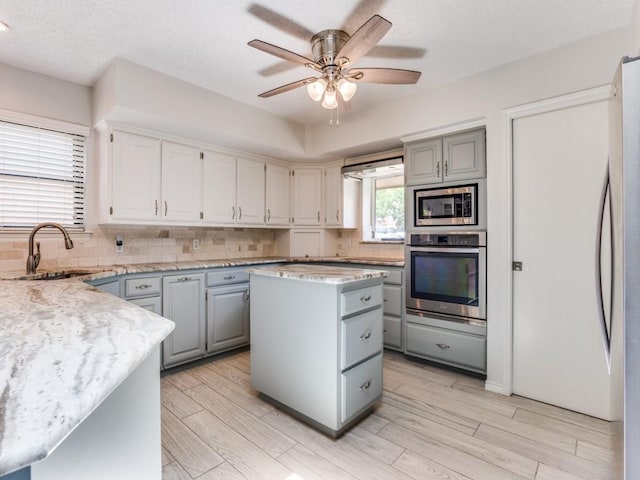 kitchen featuring appliances with stainless steel finishes, gray cabinetry, a sink, and backsplash