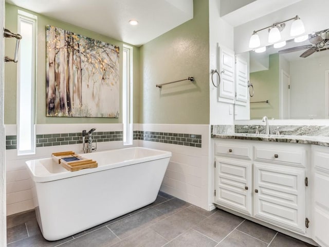 bathroom with tile walls, a freestanding bath, vanity, tile patterned flooring, and wainscoting