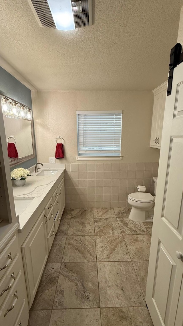 407 S Lakewood Cir, Lake Bridgeport, TX 76426 - bathroom with tile walls, a textured ceiling, toilet, double vanity, and a wainscoted wall