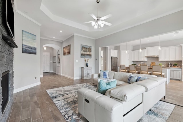 living area with ceiling fan, arched walkways, wood finished floors, a raised ceiling, and recessed lighting