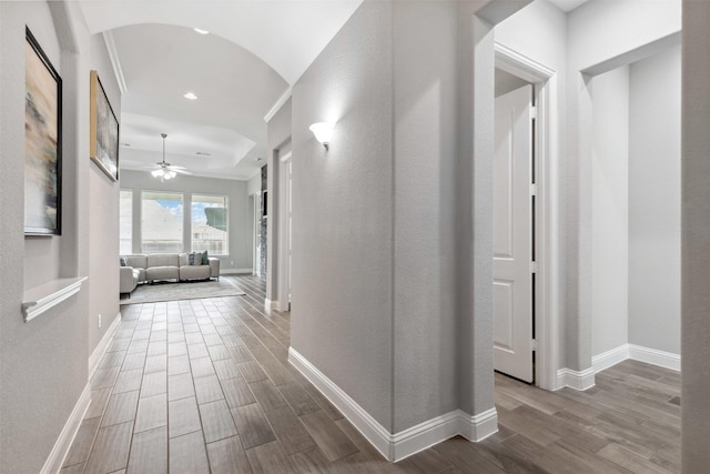 hall featuring arched walkways, baseboards, and wood finished floors