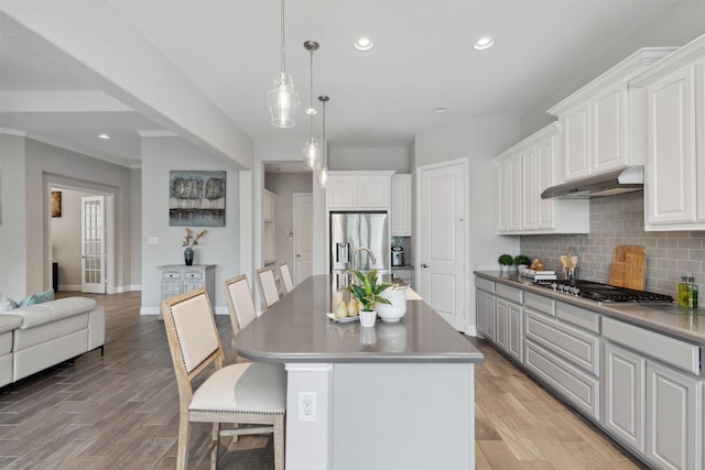 kitchen with under cabinet range hood, backsplash, appliances with stainless steel finishes, and light wood-style floors