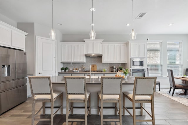 kitchen featuring a breakfast bar area, appliances with stainless steel finishes, visible vents, and tasteful backsplash