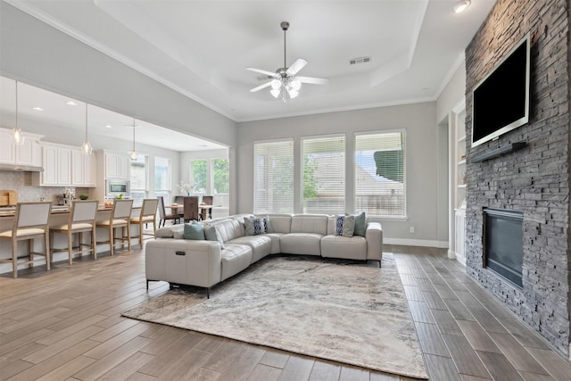 living room with a raised ceiling, ceiling fan, wood finished floors, and a fireplace