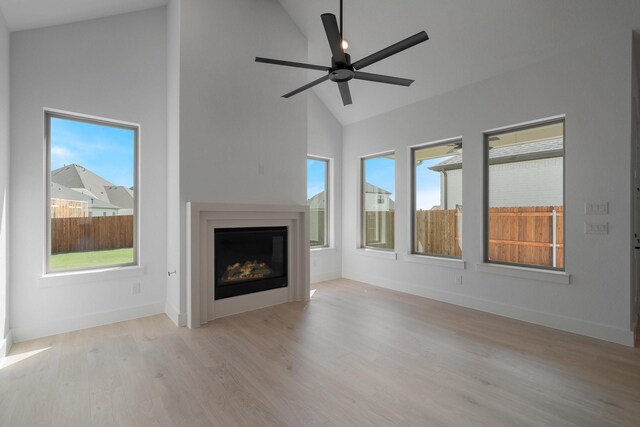unfurnished living room featuring ceiling fan, wood finished floors, high vaulted ceiling, baseboards, and a glass covered fireplace