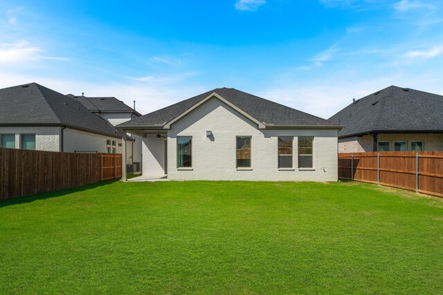 rear view of house featuring a yard, brick siding, and a fenced backyard