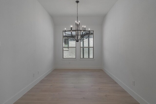 unfurnished dining area featuring baseboards, a chandelier, and light wood-style flooring