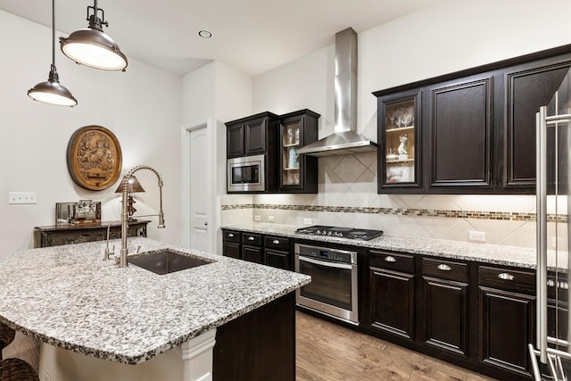 kitchen with light stone countertops, wall chimney range hood, tasteful backsplash, a sink, and appliances with stainless steel finishes