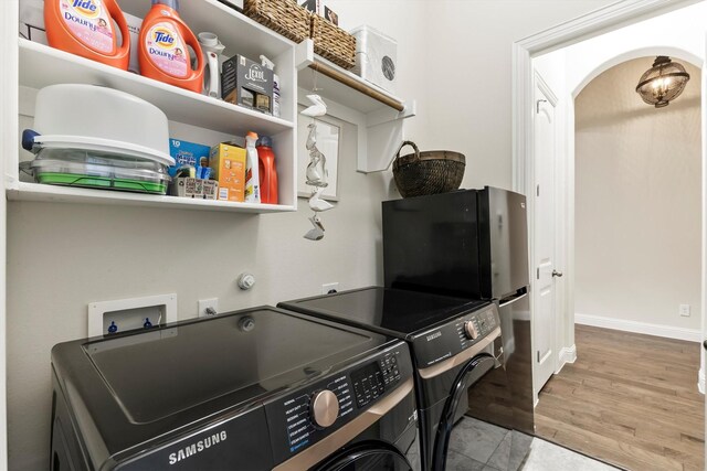 clothes washing area featuring laundry area, arched walkways, wood finished floors, baseboards, and separate washer and dryer