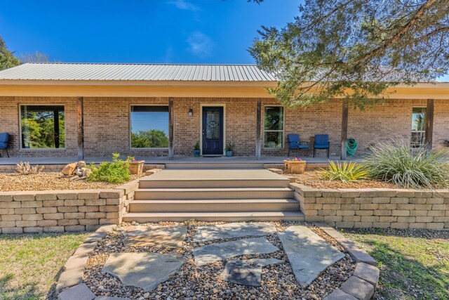 view of front of home featuring covered porch, metal roof, and brick siding